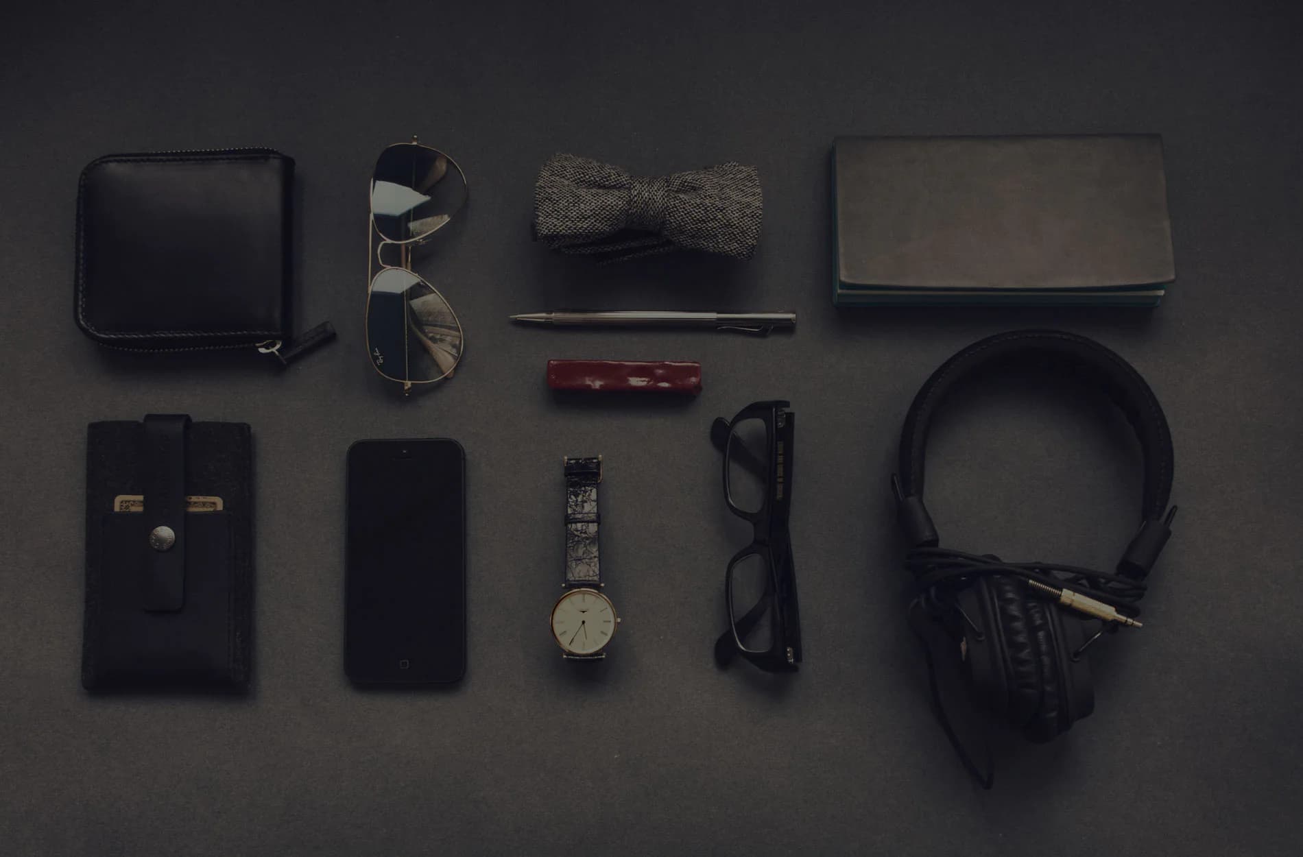 Flat lay of everyday accessories: wallet, phone, watch, glasses and headphones